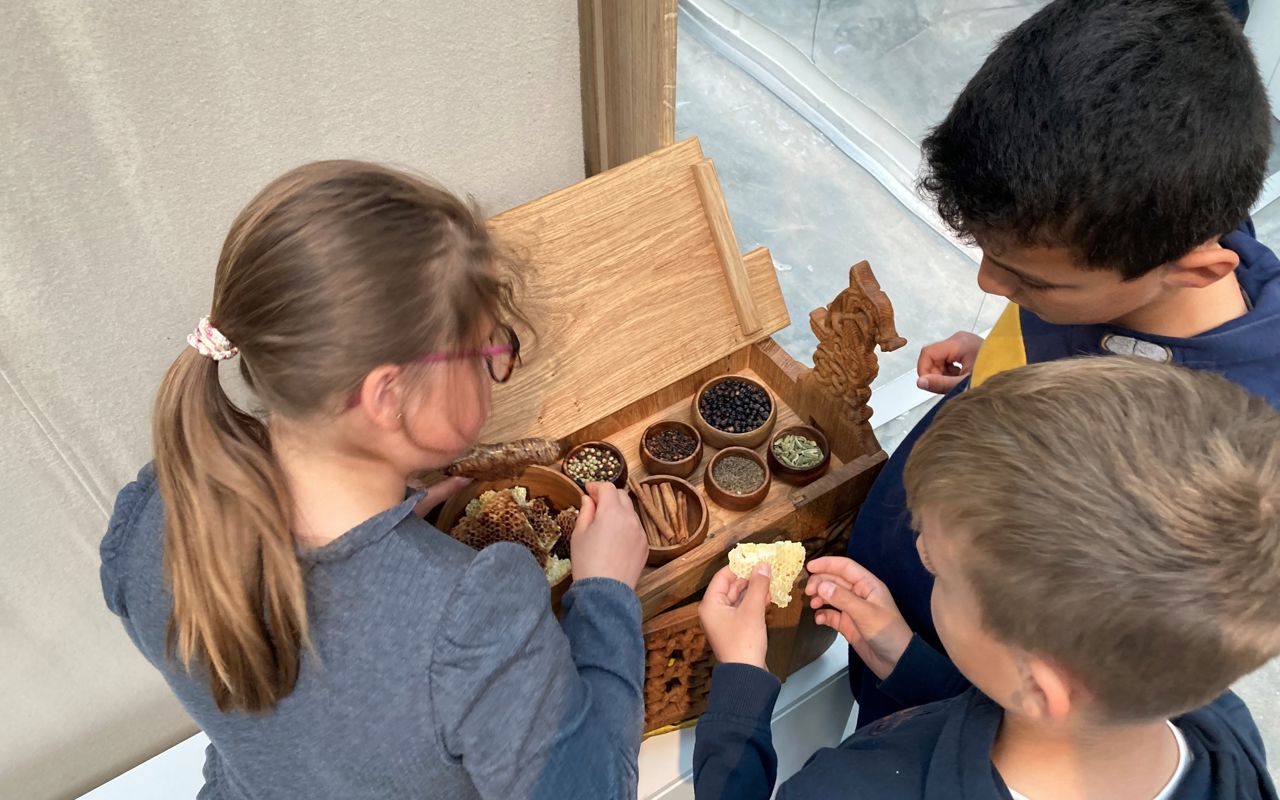 Tre børn dufter og mærker i udstillingen Magt og guld